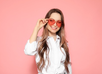 Portrait of beautiful young woman with heart shaped sunglasses on color background