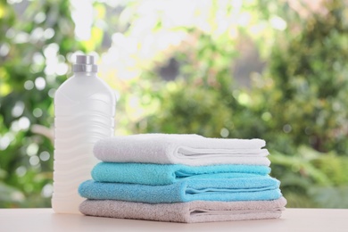 Photo of Stack of clean soft towels and laundry detergent on table against blurred background