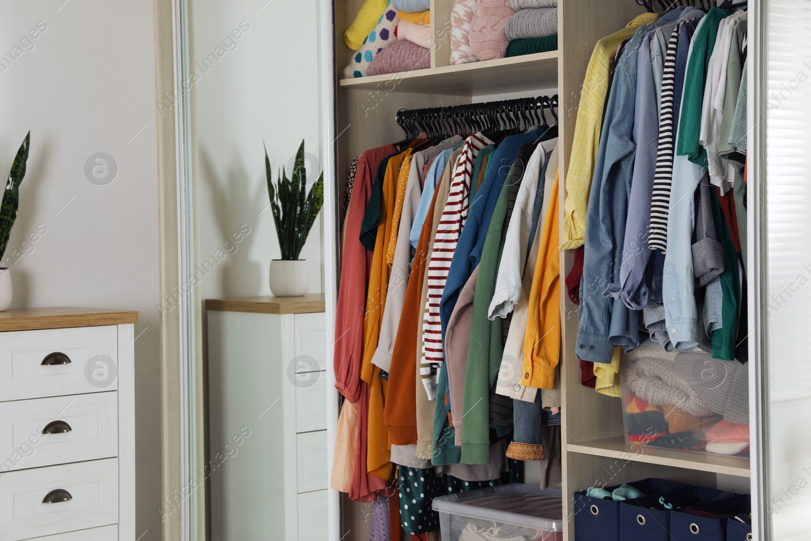 Photo of Wardrobe closet with different stylish clothes and home stuff in room. Fast fashion