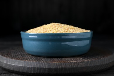 Photo of Bowl of uncooked bulgur on black wooden table, closeup