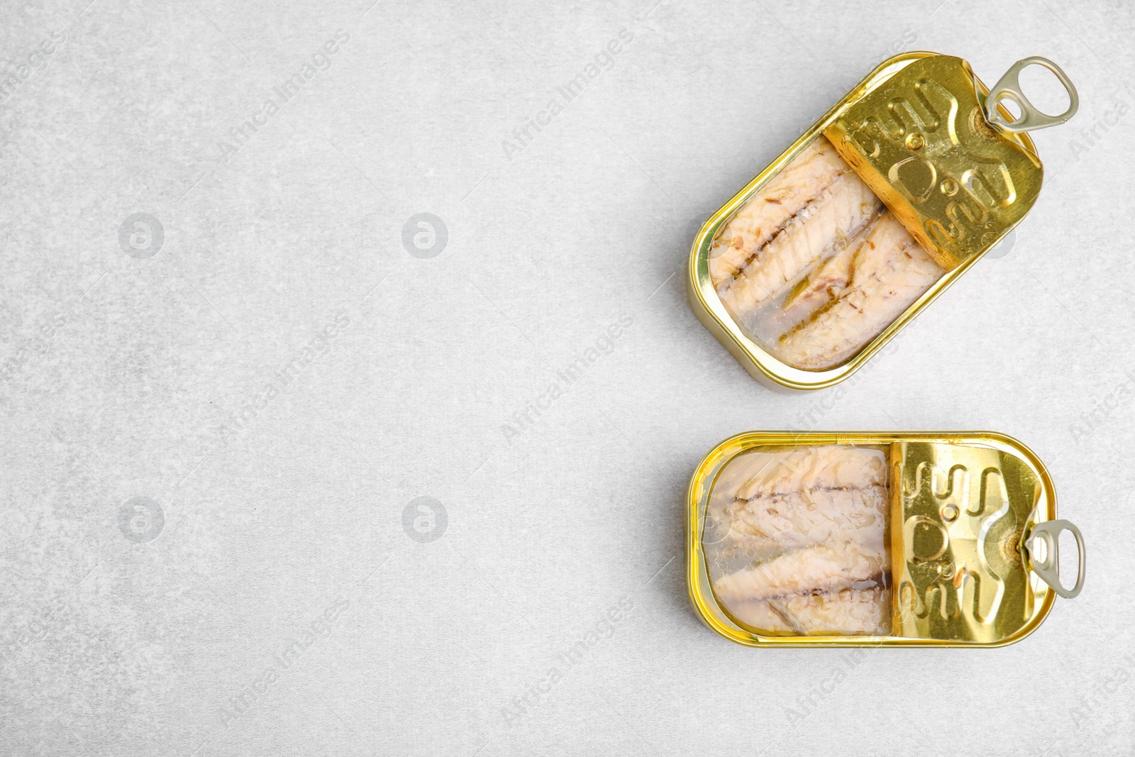 Photo of Open tin cans with mackerel fillets on grey table, flat lay. Space for text
