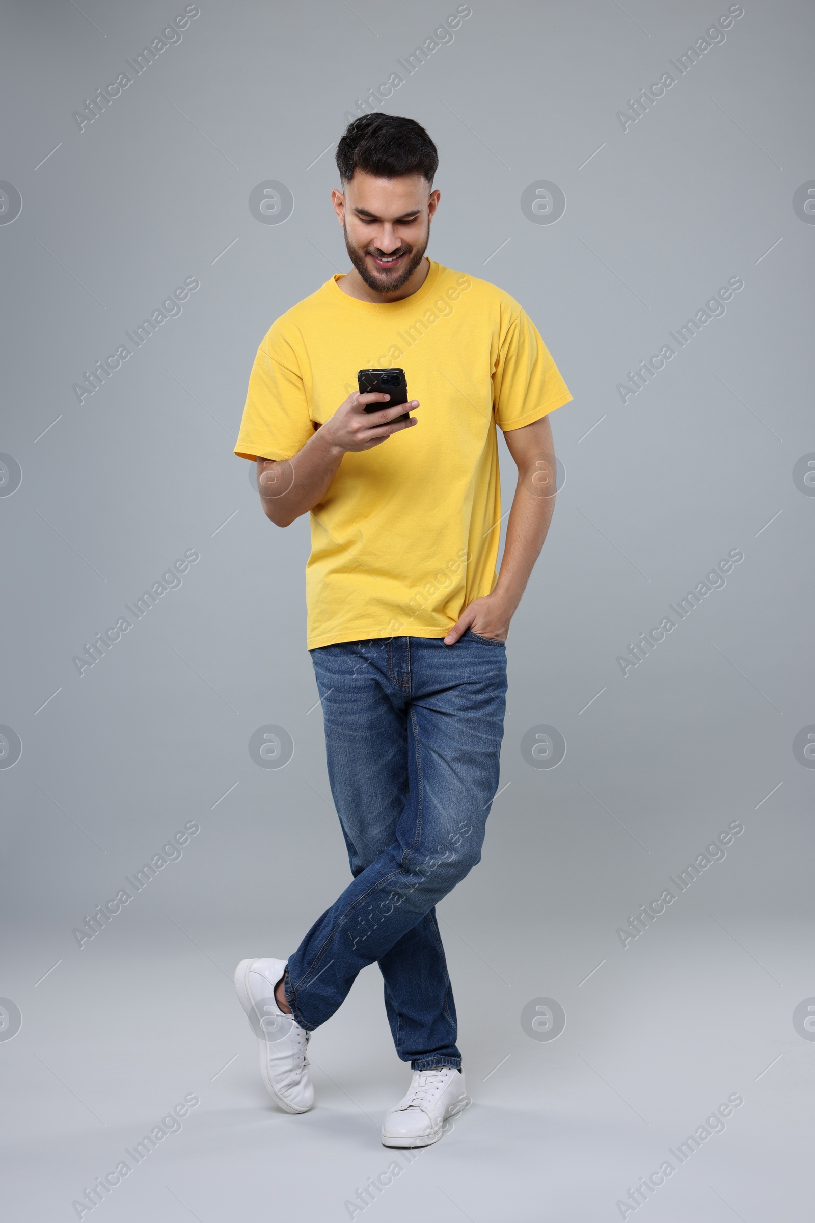 Photo of Happy young man using smartphone on grey background