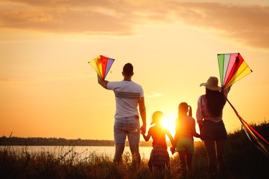 Photo of Parents and their children playing with kites outdoors at sunset, back view. Spending time in nature