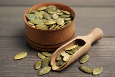 Photo of Bowl and scoop with pumpkin seeds on wooden table, closeup