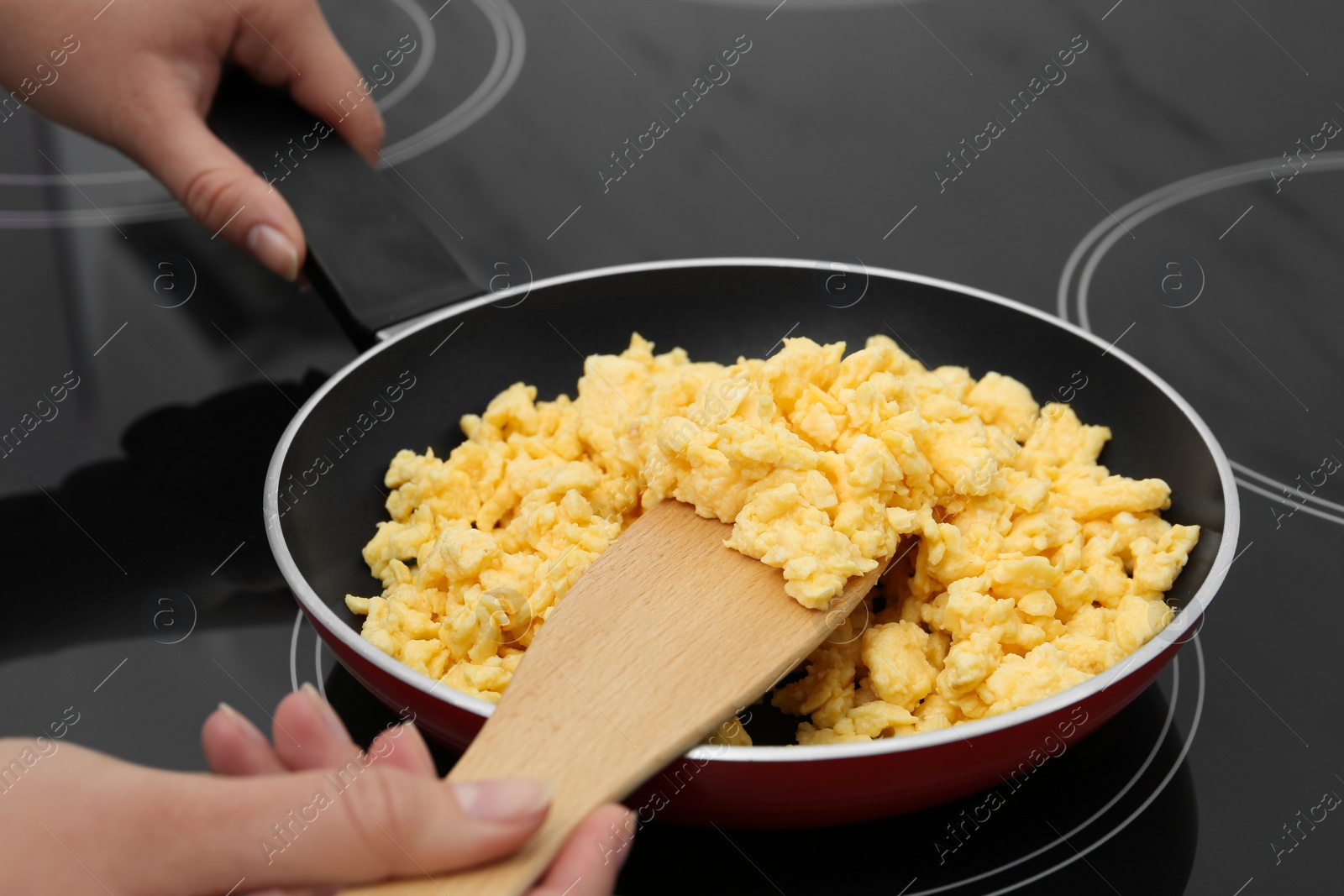 Photo of Woman cooking tasty scrambled eggs in frying pan on stove, closeup
