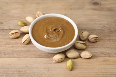 Delicious nut butter in bowl and pistachios on wooden table