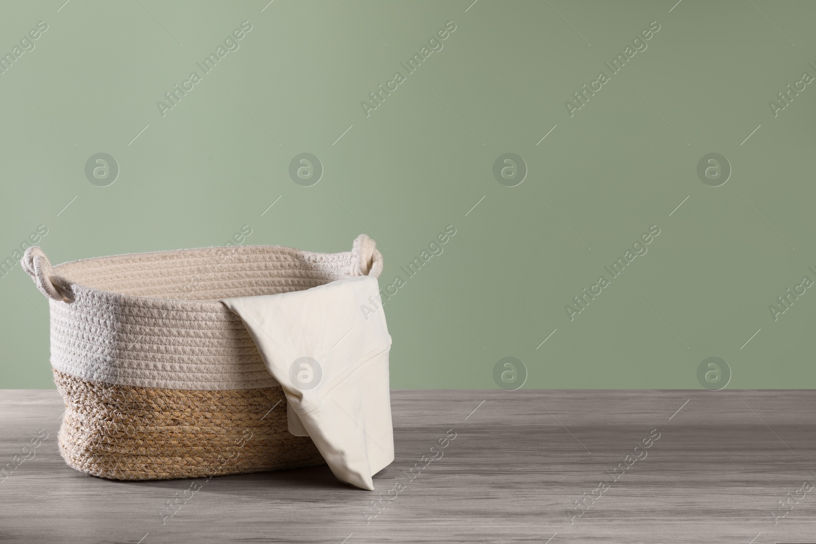 Photo of Wicker laundry basket with clothes near light green wall. Space for text