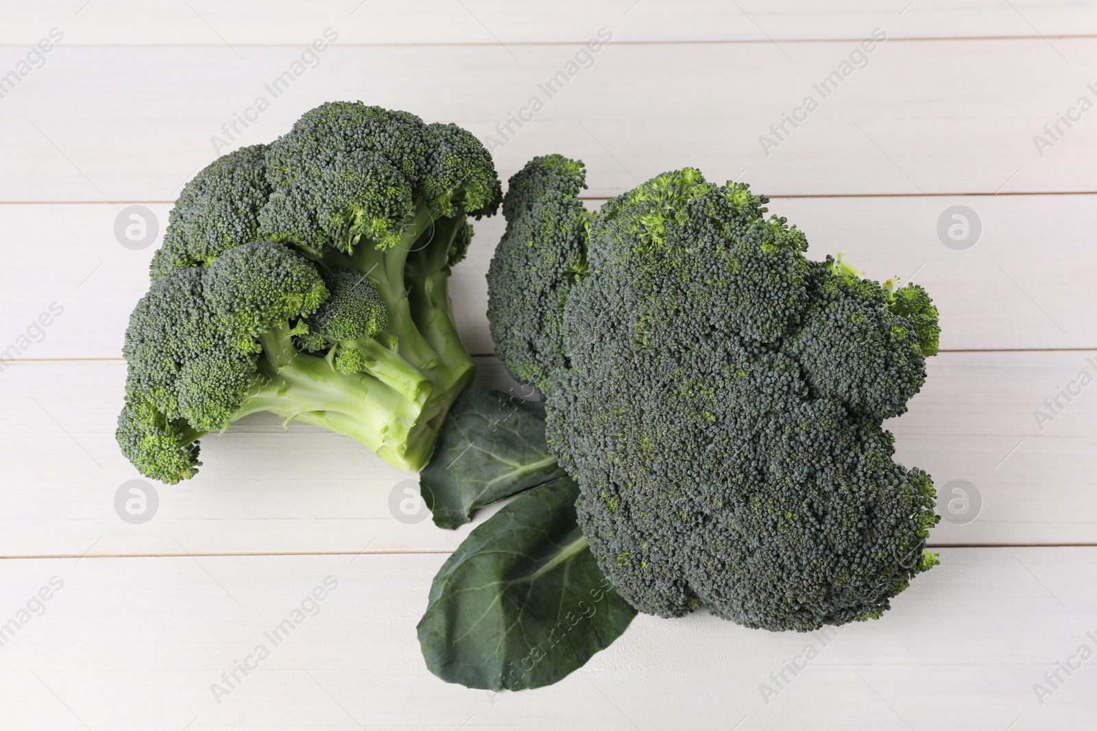 Photo of Fresh raw broccoli on white wooden table, top view