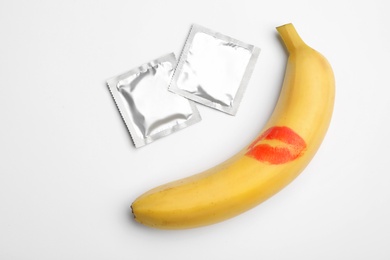 Photo of Condoms and banana with lipstick kiss mark on white background, top view. Safe sex