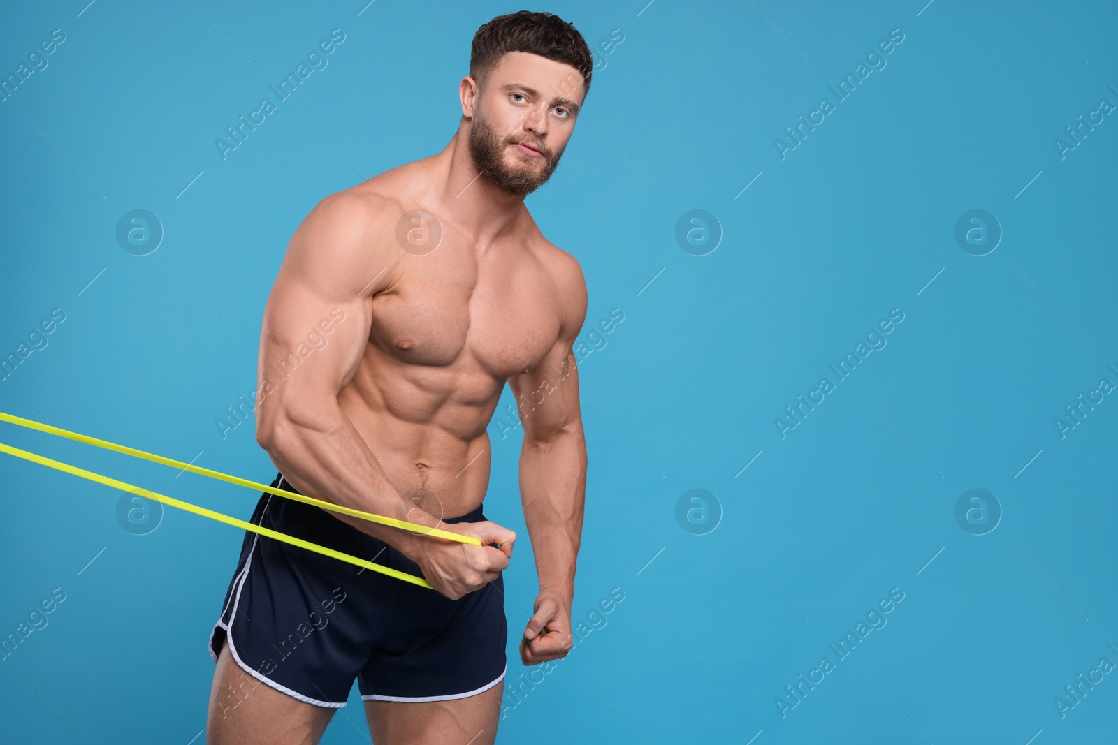 Photo of Young man exercising with elastic resistance band on light blue background. Space for text