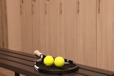 Tennis racket and balls on wooden bench in locker room