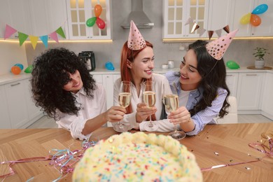 Happy young women with tasty cake and glasses of sparkling wine celebrating birthday in kitchen