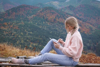 Photo of Young woman drawing on tablet in mountains, space for text