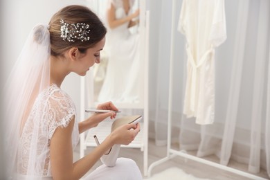 Photo of Young bride writing on her shoe indoors, space for text. Wedding superstition