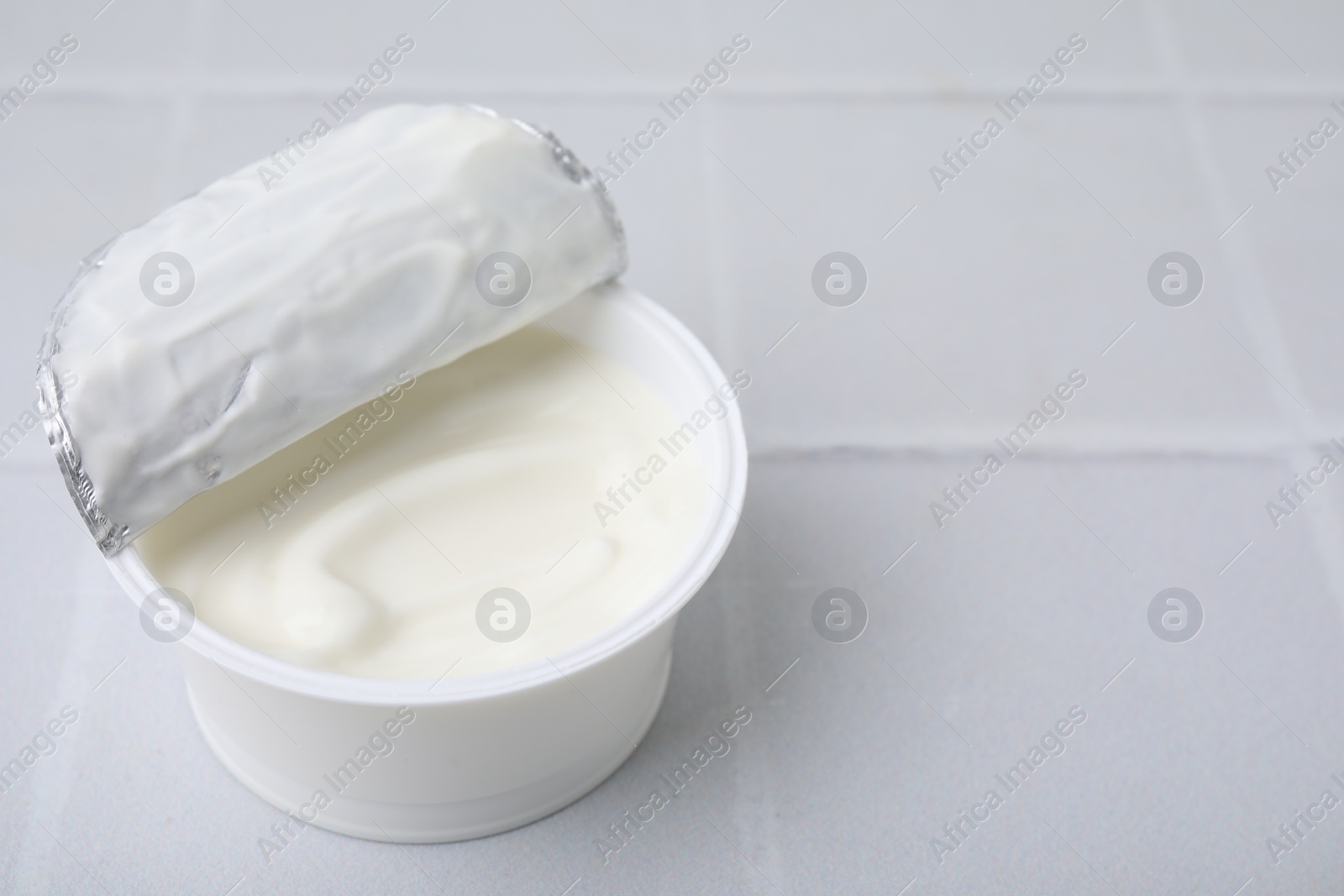 Photo of Delicious natural yogurt in plastic cup on white tiled table, closeup. Space for text