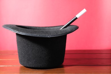 Black top hat and wand on wooden table, space for text. Magician equipment