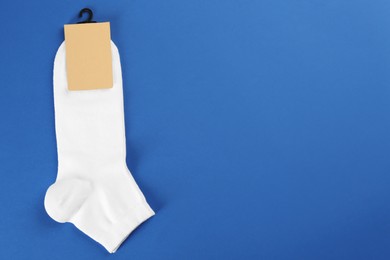 Photo of Pair of white cotton socks on blue background, top view. Space for text