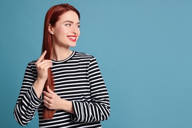 Happy woman with red dyed hair on light blue background, space for text