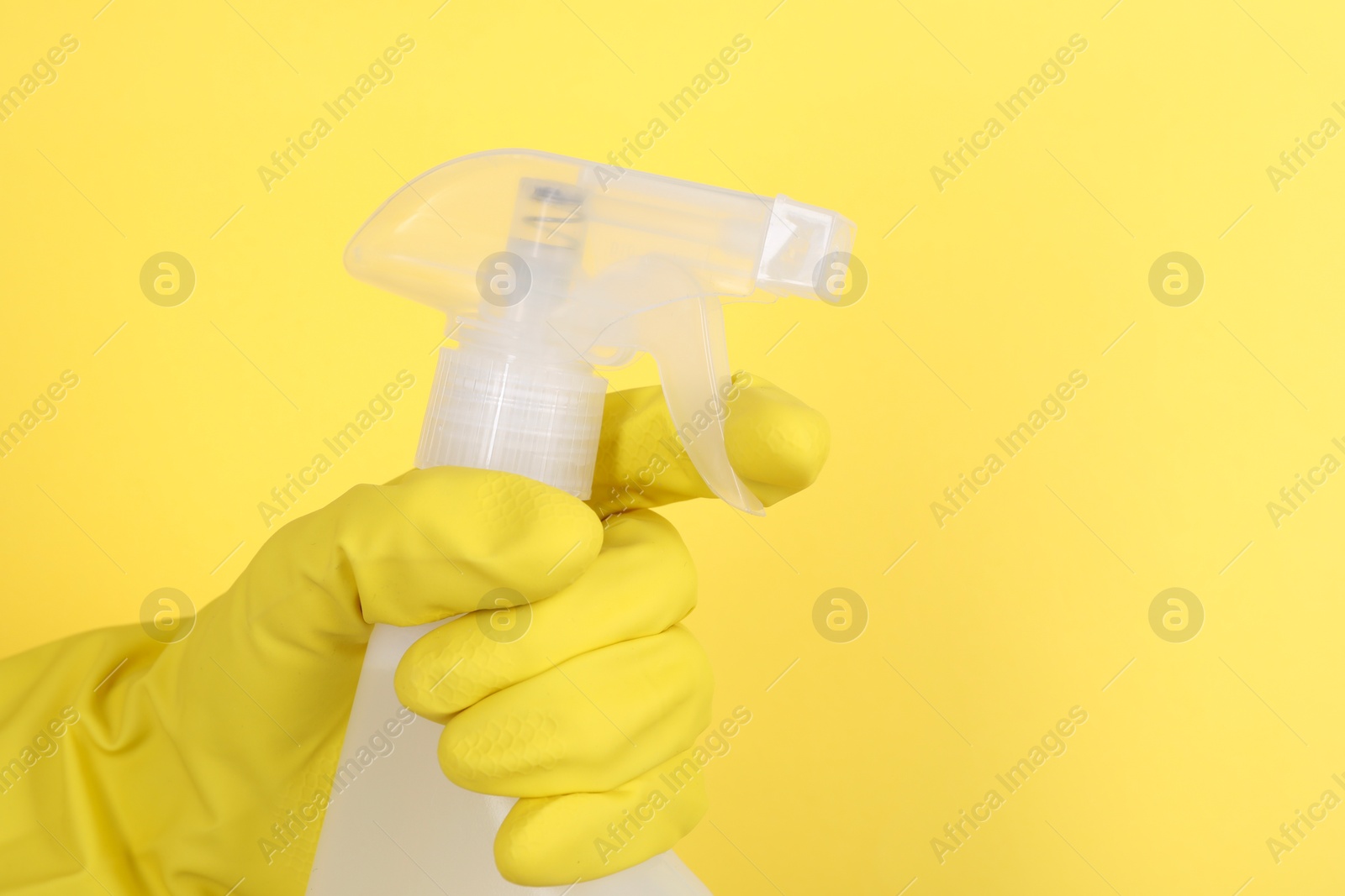 Photo of Woman holding plastic spray bottle on yellow background, closeup. Space for text