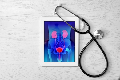 Tablet displaying urinary system and stethoscope on wooden background. Urology concept