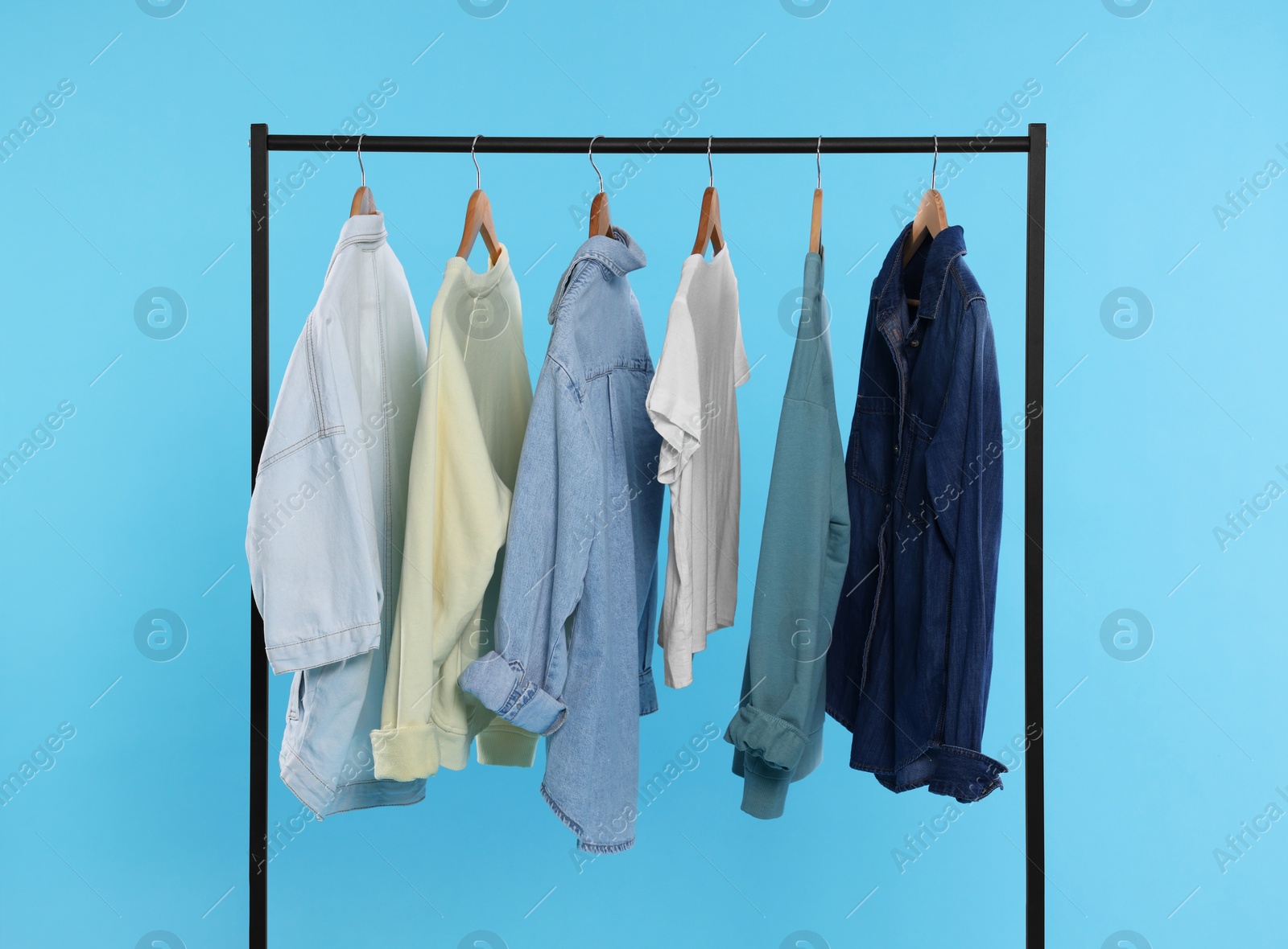 Photo of Rack with stylish clothes on wooden hangers against light blue background