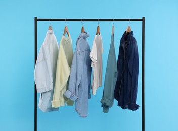 Photo of Rack with stylish clothes on wooden hangers against light blue background