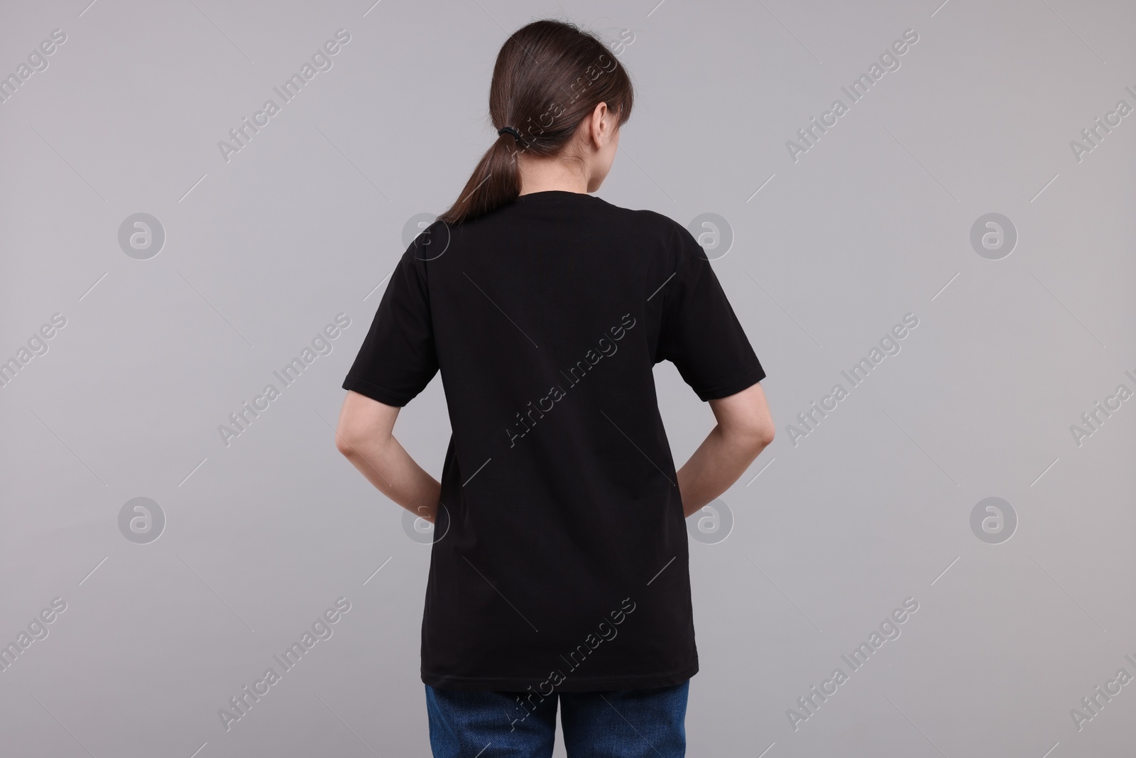 Photo of Woman in stylish black t-shirt light grey on background, back view