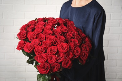 Woman holding luxury bouquet of fresh red roses near white brick wall, closeup