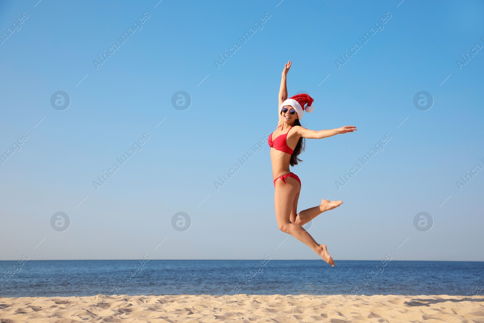 Photo of Beautiful young woman in Santa hat and bikini having fun on beach, space for text. Christmas vacation