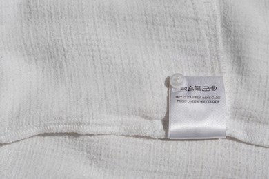 Photo of Clothing label with instruction on white garment, top view. Space for text