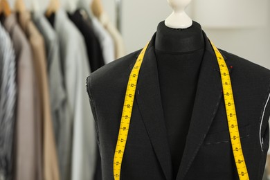 Mannequin with unfinished jacket and measuring tape in tailor shop, closeup. Space for text