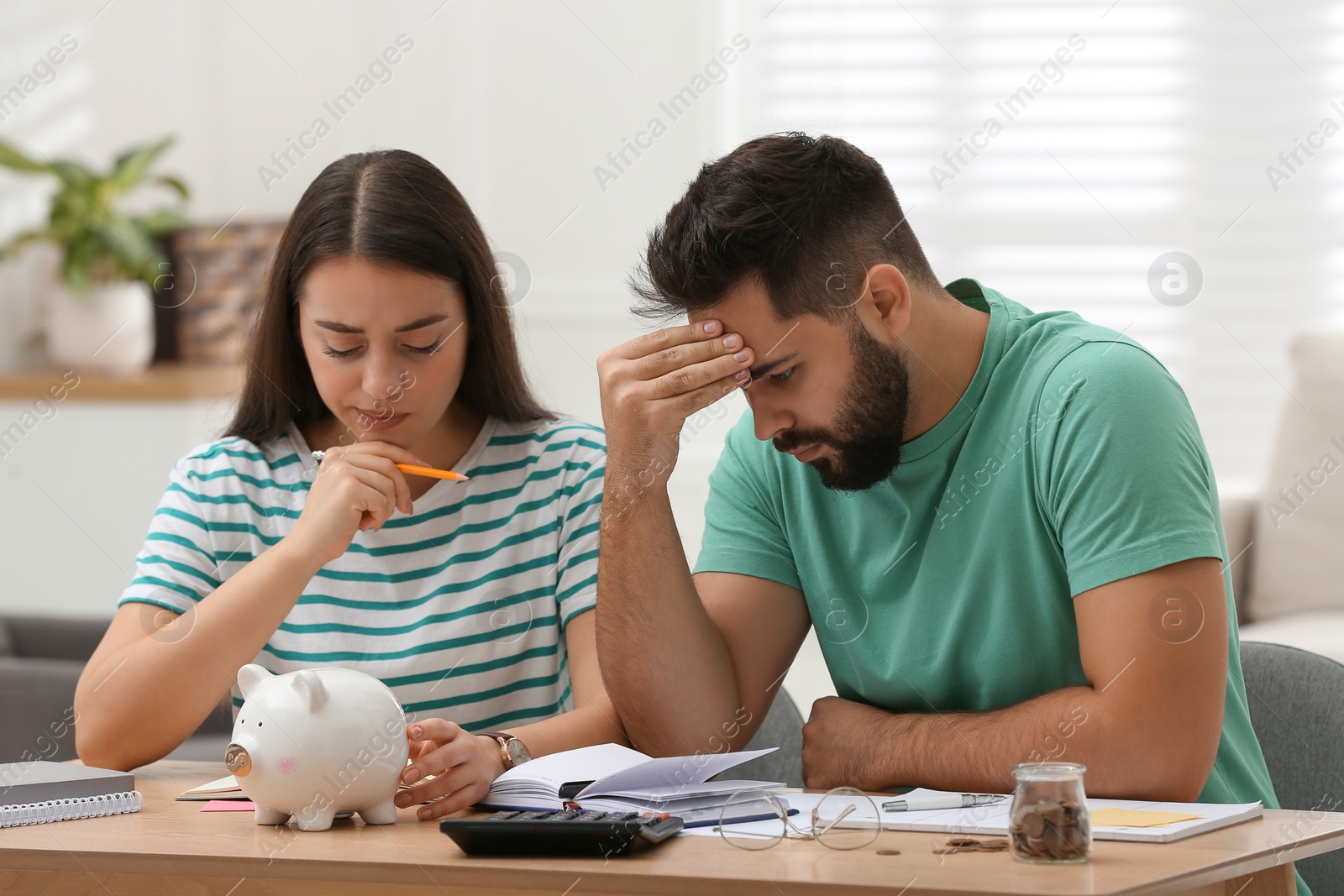 Photo of Worried young couple planning family budget at wooden table indoors