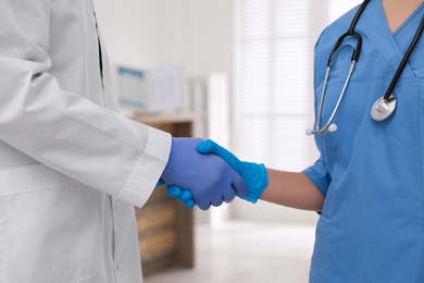 Doctors in medical gloves giving handshake at hospital, closeup