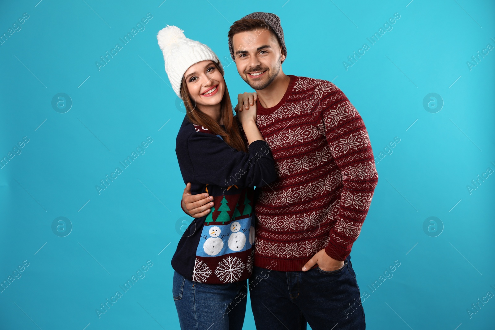 Photo of Couple wearing Christmas sweaters and hats on blue background