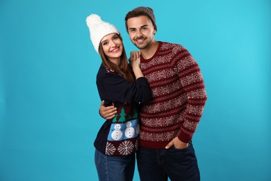 Couple wearing Christmas sweaters and hats on blue background