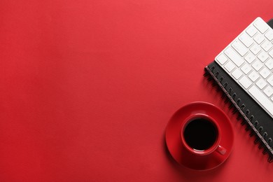 Cup with aromatic coffee, notepad and keyboard on red background, flat lay. Space for text