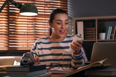 Emotional young woman with energy drink studying at home