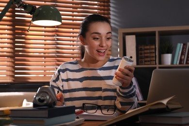 Photo of Emotional young woman with energy drink studying at home