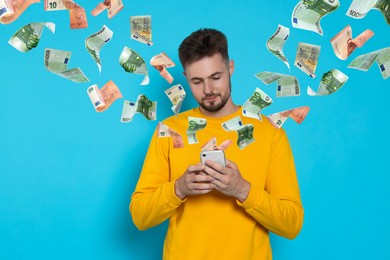 Image of Online payment. Man buying something using mobile phone on light blue background. Euro banknotes flying out of gadget demonstrating process of money transaction
