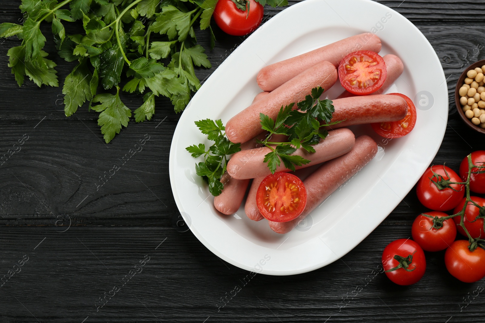 Photo of Delicious vegetarian sausages with parsley, tomatoes and soybeans on black wooden table, flat lay