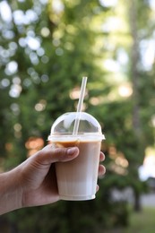 Photo of Man holding plastic takeaway cup of delicious iced coffee outdoors, closeup