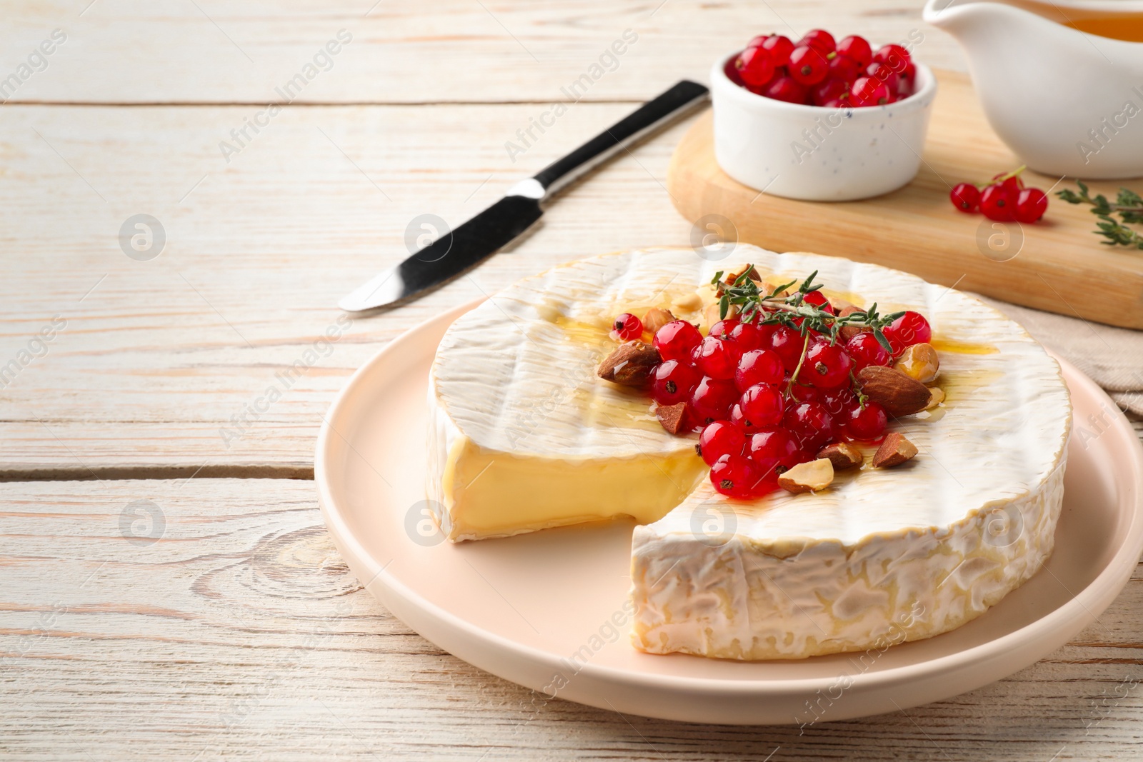 Photo of Brie cheese served with almonds, red currants and honey on white wooden table. Space for text