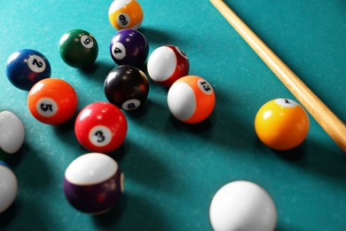 Many colorful billiard balls and cue on green table, closeup
