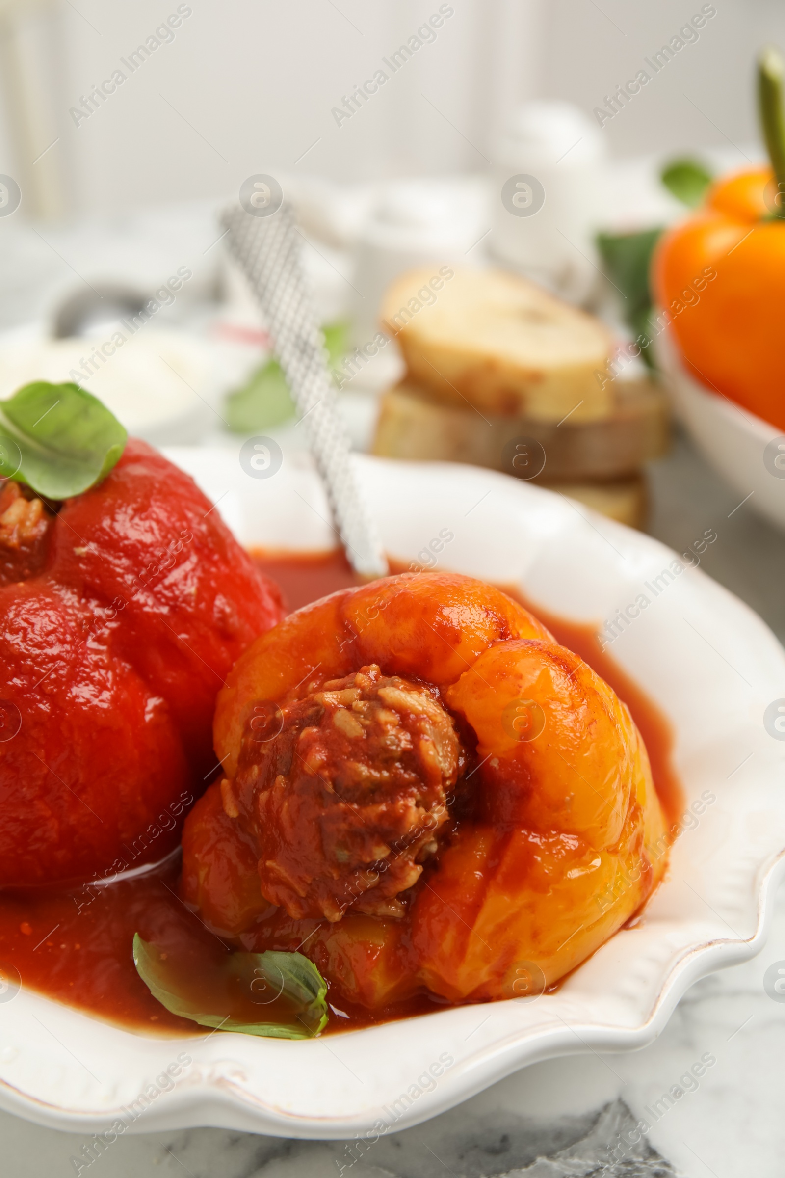 Photo of Delicious stuffed peppers with basil in bowl on white marble table, closeup