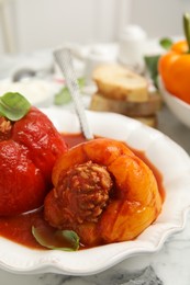 Photo of Delicious stuffed peppers with basil in bowl on white marble table, closeup