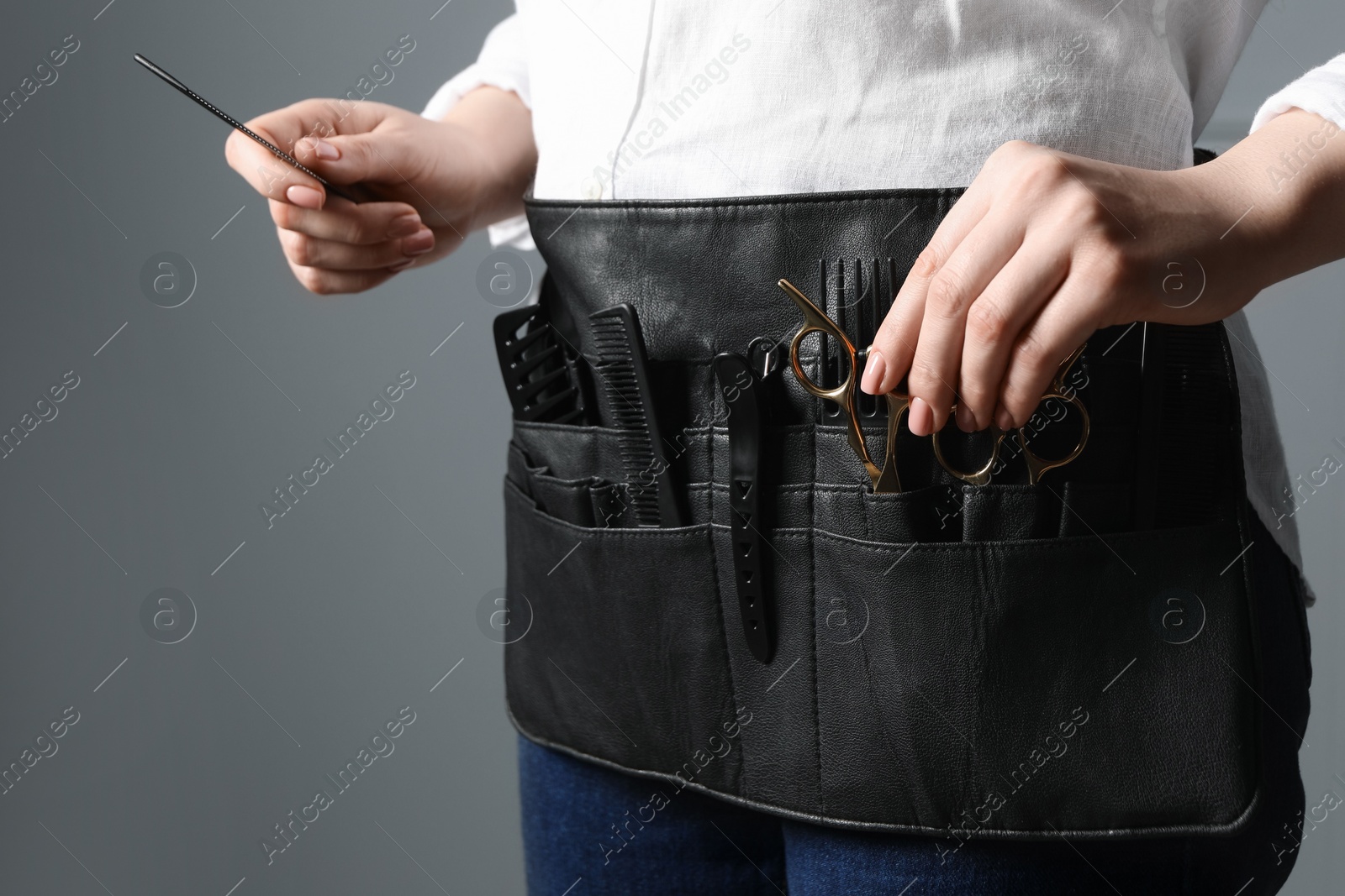 Photo of Hairstylist with professional tools in waist pouch on grey background, closeup