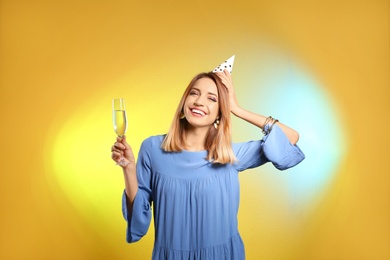 Portrait of happy woman with party hat and champagne in glass on color background