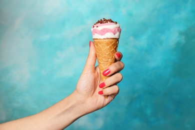 Photo of Woman holding yummy ice cream on color background. Focus on hand