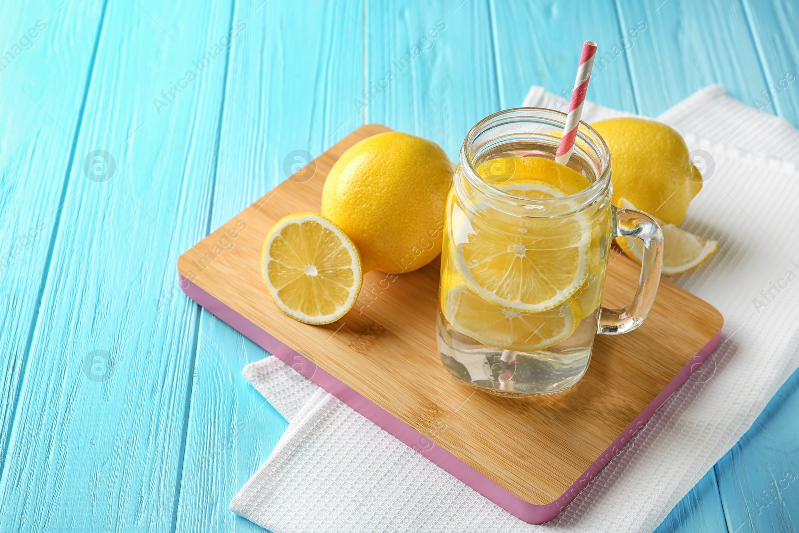 Photo of Mason jar with lemon water and fresh fruits on wooden board