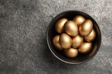 Shiny golden eggs in bowl on grey table, top view. Space for text